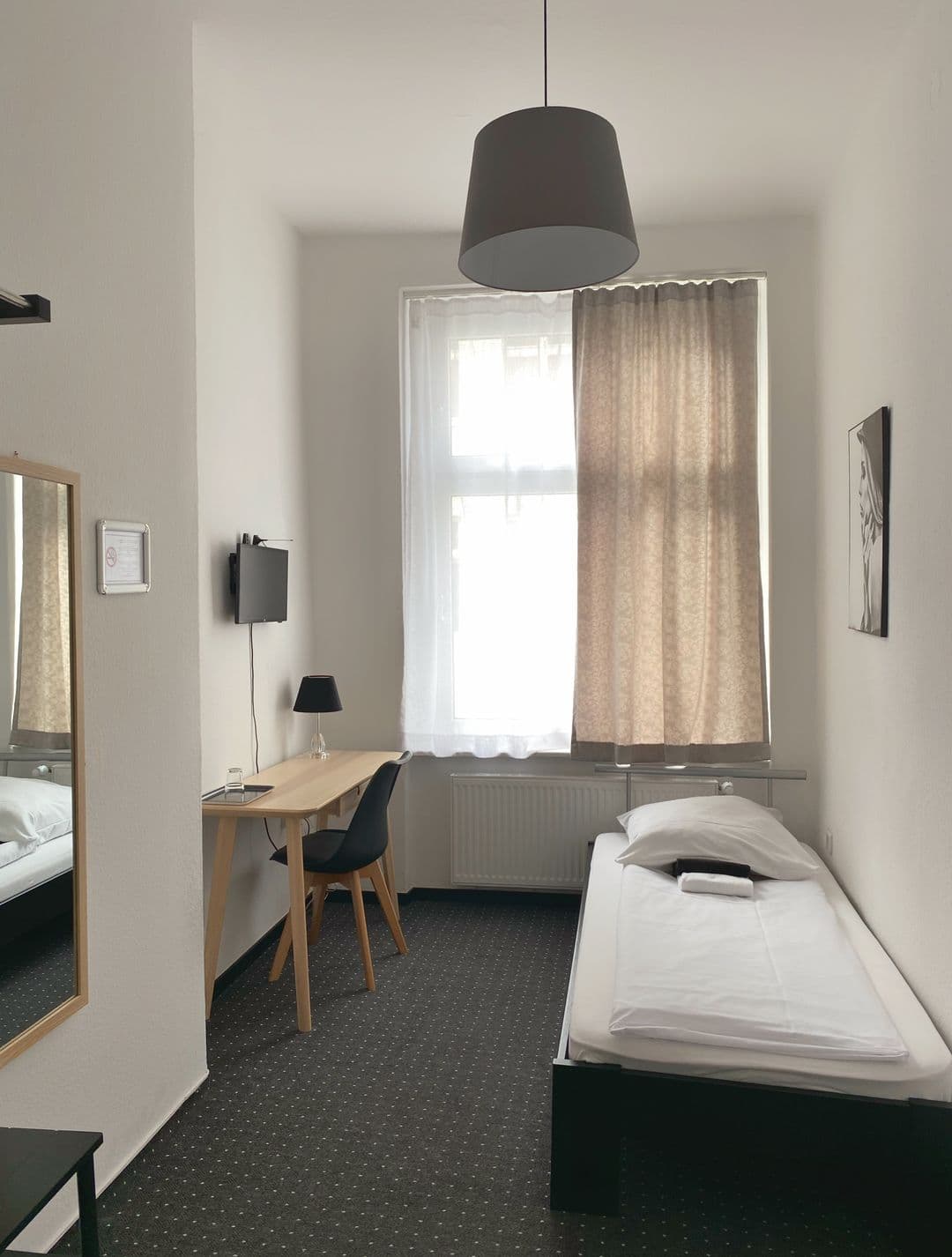 Einzelzimmer mit Bett am Fenster und Wandspiegel