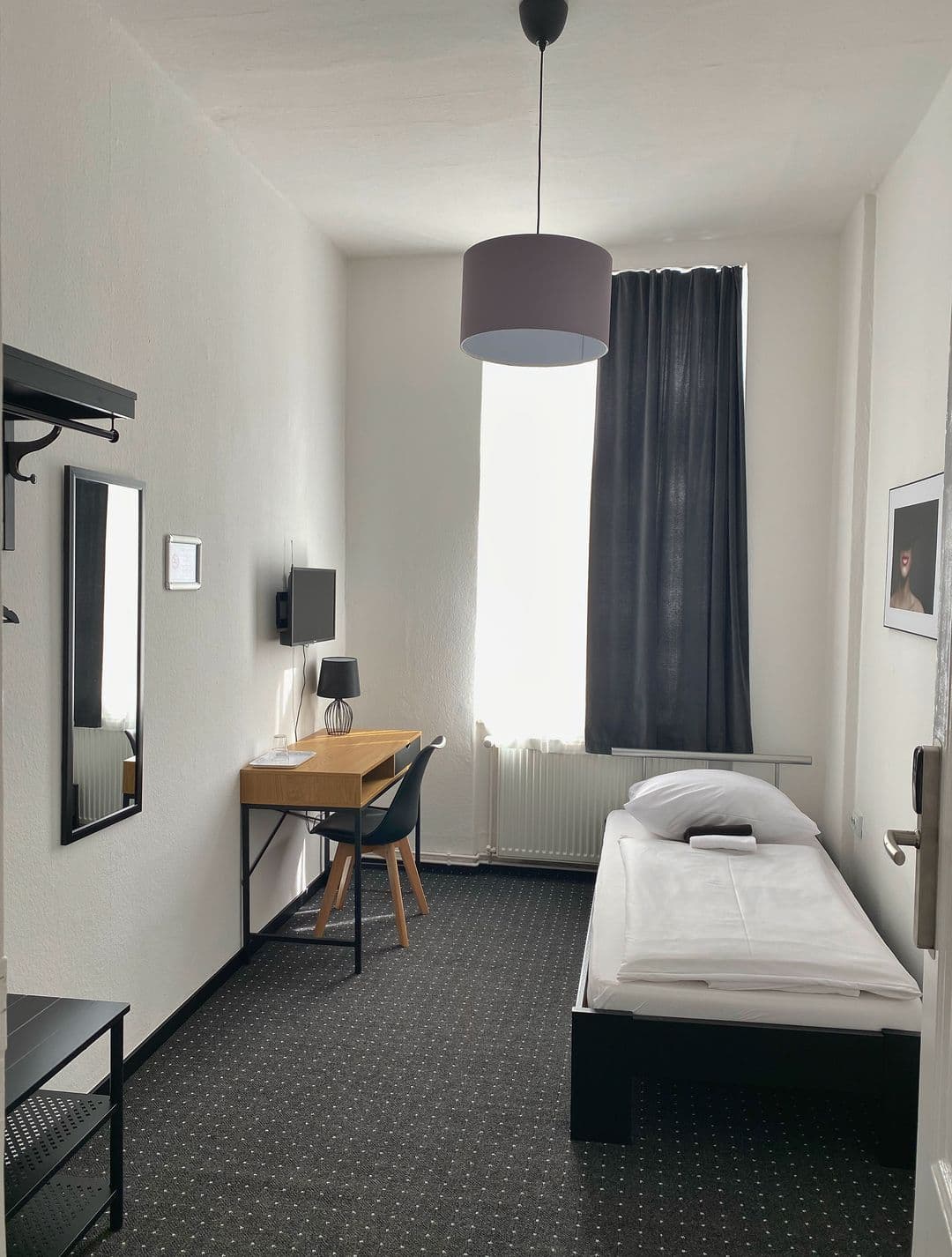 Einzelzimmer mit Schreibtisch, Stuhl und Bett vor dem Fenster